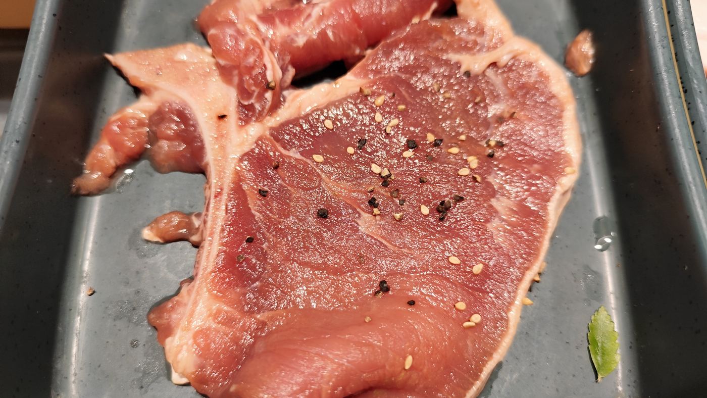 A raw T-bone steak seasoned on a tray