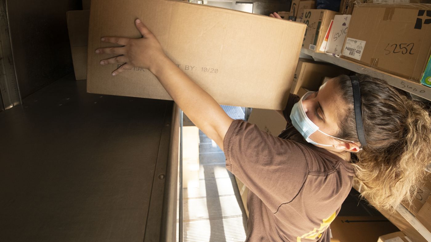A worker lifting a box into a delivery truck at a loading dock